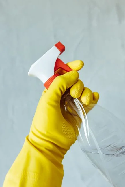 Anonymous male wearing yellow latex gloves and dark t shirt wiping mirror in bathroom with paper napkin